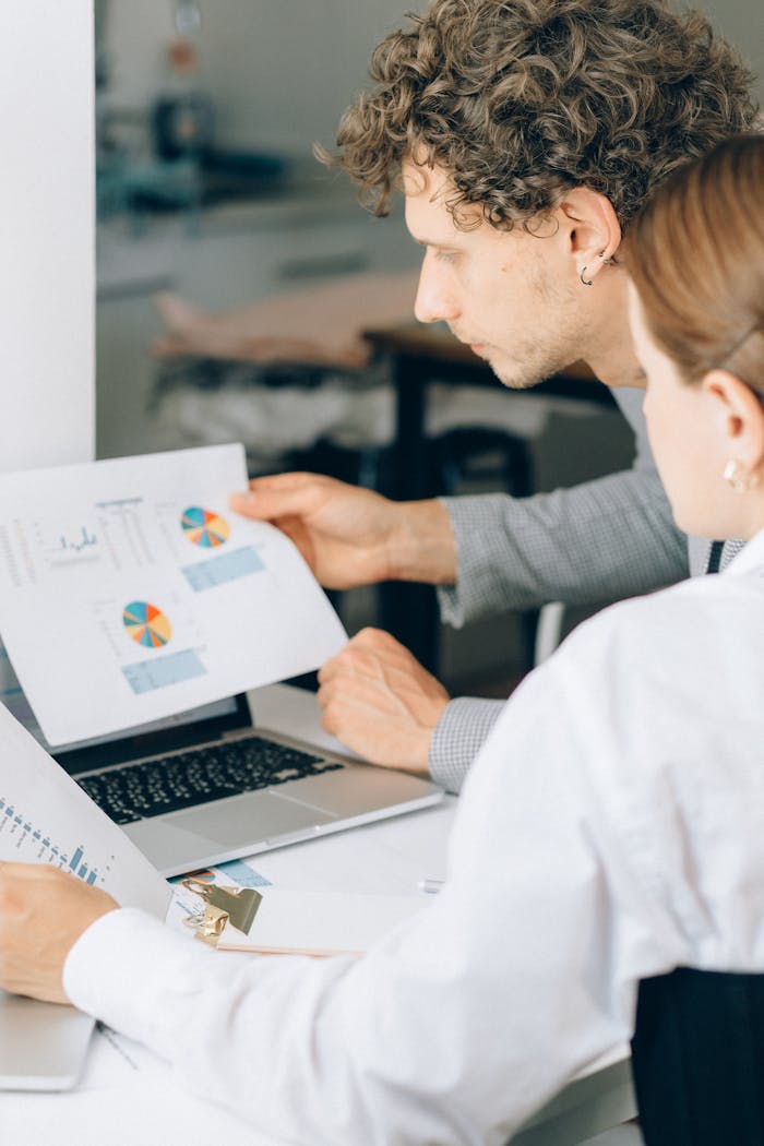 Two business professionals reviewing financial charts and graphs in a modern office setting.